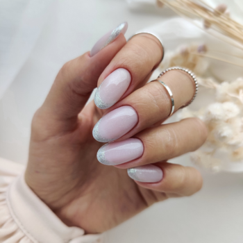 Zbliżenie dłoni z owalnymi paznokciami, prezentującymi brokatowy french manicure z delikatnymi, błękitnymi końcówkami.