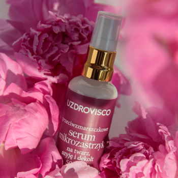 Uzdrovisco serum przeciwzmarszczkowe "Mikrozastrzyk" w białej butelce, ze złotym dozownikiem, wśród różowych piwonii.