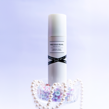 Biały flakon mgiełki perfumowanej Precious Pearl z etykietą, otoczony perłami. Tropikalny zapach, widok frontalny.