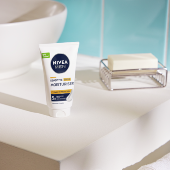 Biała tubka NIVEA MEN Sensitive Moisturiser SPF 15 do skóry wrażliwej na białym blacie łazienkowym.