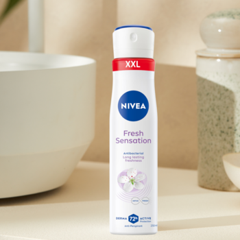 Biały antyperspirant NIVEA Fresh Sensation XXL w sprayu 72h, z fioletowym kwiatem, na jasnym tle łazienki.