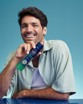 Antyperspirant NIVEA MEN Fresh Sensation w niebieskim sprayu, trzymany przez uśmiechniętego mężczyznę.