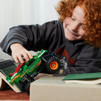 Uśmiechnięty chłopiec bawi się zielonym pojazdem LEGO Technic Monster Jam z silnikiem pull-back i smoczymi detalami.