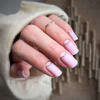 Zbliżenie dłoni z manicure: różowe paznokcie ombre z białymi końcówkami i złotym wzorem półksiężyca, delikatny pierścionek.