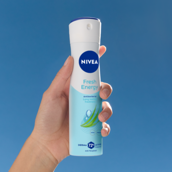 Biało-niebieski antyperspirant NIVEA Fresh Energy z trawą cytrynową, trzymany w dłoni na tle błękitnego nieba.