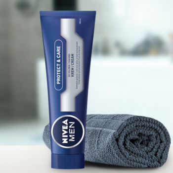 Niebieska tuba NIVEA MEN Protect & Care krem do golenia, z srebrną etykietą, obok szarego ręcznika.