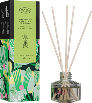 Dekoracyjny odświeżacz powietrza Trawa Orientu z Akacją. Czarne opakowanie w liście, obok szklany dyfuzor z patyczkami.