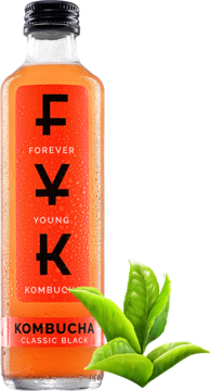 Butelka Kombuchy Forever Young Classic Black z bursztynowym płynem i czerwoną etykietą, obok świeże liście herbaty.