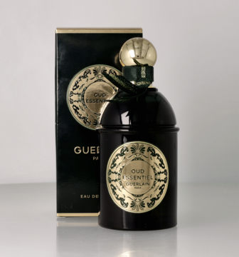 Guerlain Oud Essentiel, ciemny flakon perfum ze złotymi detalami i zieloną wstążką, z pudełkiem w tle.