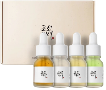 Beauty of Joseon Hanbang Serum Kit: 4 miniaturowe butelki z różnobarwnymi serami, przed beżowym pudełkiem.