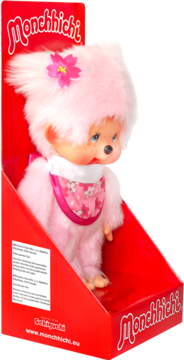 Pluszowa lalka Monchhichi w jaskrawo różowym futerku z kwiatkiem, śliniakiem, w czerwonym opakowaniu detalicznym.