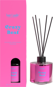 Różowy dyfuzor zapachowy Your Candle 'Crazy Beaf' z czarnymi patyczkami, obok pasującego, jaskrawego opakowania.