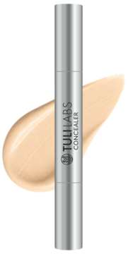 Korektor pod oczy Tuli Labs w srebrnej tubce, leżący na beżowej smudze produktu, widok z góry.