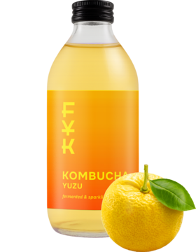 Butelka FOREVER YOUNG KOMBUCHA Yuzu, przejrzysta z pomarańczową etykietą, obok leży owoc yuzu z liściem.