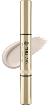 Złoty TULI LABS EYESHADOW STICK i kremowy, błyszczący swatch cienia do powiek na czarnym tle.