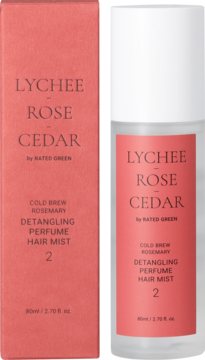 Różowe pudełko i przezroczysta butelka Rated Green Lychee-Rose-Cedar Detangling Perfume Hair Mist, stojące na ciemnym tle.