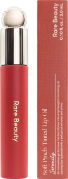 Czerwony Rare Beauty Soft Pinch Tinted Lip Oil Serenity w tubce ze srebrną nakrętką, obok pudełka z opisem.