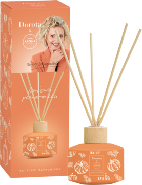 Pomarańczowy dyfuzor zapachowy z patyczkami i ilustracjami dyni, obok pudełko z wizerunkiem kobiety i 'Aroma pomarańcza'.