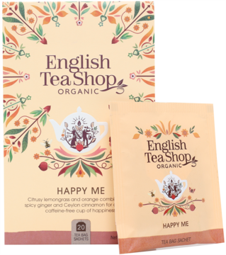Beżowe pudełko herbaty English Tea Shop Organic Happy Me i saszetka, z ilustracjami czajniczka i liści.