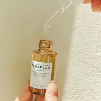 Zbliżenie kojącej ampułki Skin1004 Madagascar Centella w bursztynowej butelce, kropla spada z pipety.