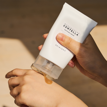 Biała tubka SKIN1004 Centella kremu do twarzy, brązowa ciecz dozowana na dłoń, zbliżenie.