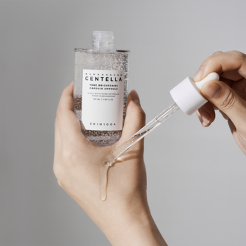Serum rozjaśniające Skin1004 z Centellą na przebarwienia, w szklanej butelce, krople spływają na dłoń.