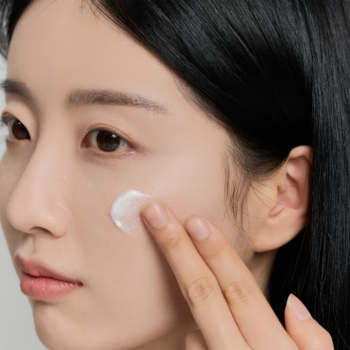 Zbliżenie na kobietę delikatnie aplikującą biały krem Madagascar Centella Tone Brightening Capsule Cream.