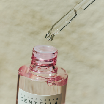 Skin1004 Madagascar Centella Poremizing Ampoule, zbliżenie na różowe serum w butelce z kroplą z pipety.