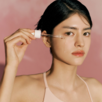 Kobieta aplikuje serum zmniejszające pory pipetą. Kropla na policzku. Produkt dla skóry tłustej i mieszanej.