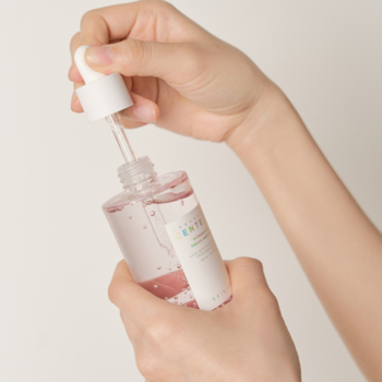 Serum zmniejszające pory, różowe, w szklanej butelce z pipetą, dłonie wkładają zakraplacz.
