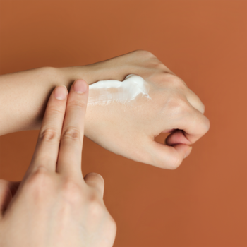 Bliskie ujęcie dłoni nakładającej biały, odżywczy krem Skin1004 Madagascar Centella na skórę dłoni.