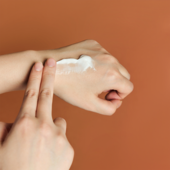 Zbliżenie dłoni aplikującej biały, odżywczy krem Skin1004 Madagascar Centella Probio-CICA Enrich Cream.