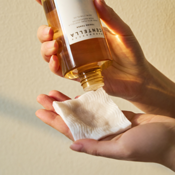 Zbliżenie na dłoń wylewającą złuszczający tonik Skin 1004 Madagascar Centella na wacik z bursztynowej butelki.