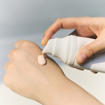 Ręka wyciskająca beżowy krem ochronny SPF 50+ z białej butelki z pompką na nadgarstek.