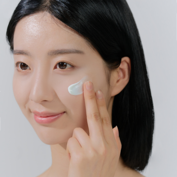 Młoda kobieta nakłada na policzek lekki krem przeciwsłoneczny Skin1004 Hyalu-Cica Water-Fit Sun Serum.