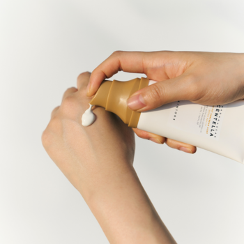 Dłonie aplikujące Skin1004 Madagascar Centella Air-Fit Suncream Light SPF30, krem wyciskany z beżowej tubki na skórę.