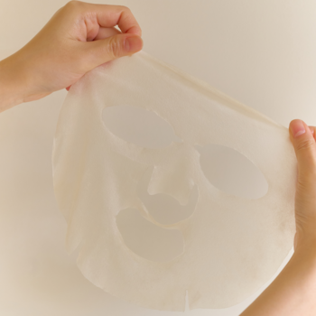 Hydrożelowa maska do twarzy w płachcie, trzymana przez dłonie, z widocznymi otworami na oczy i usta, gotowa do aplikacji.