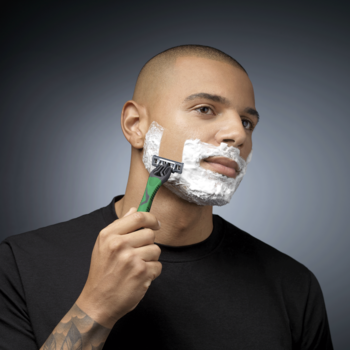 Mężczyzna z pianką na twarzy goli się maszynką Wilkinson Quattro Essentials 4 z aloesem dla wrażliwej skóry.