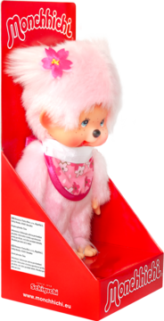 Pluszowa lalka Monchhichi w jaskrawo różowym futerku z kwiatkiem, śliniakiem, w czerwonym opakowaniu detalicznym.