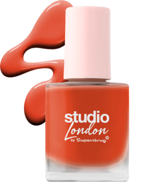 Studio London koralowy lakier do paznokci z jasnoróżową nakrętką, butelka stoi obok dużej, rozlanej kropli.