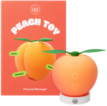 Pomarańczowy masażer osobisty w kształcie brzoskwini z zielonymi listkami, na białej podstawce obok opakowania Peach Toy.