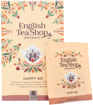 Beżowe pudełko herbaty English Tea Shop Organic Happy Me i saszetka, z ilustracjami czajniczka i liści.