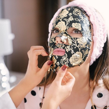 Kobieta nakłada czarno-złotą koreańską maskę w płachcie no:hj z perłami, modelującą owal twarzy.