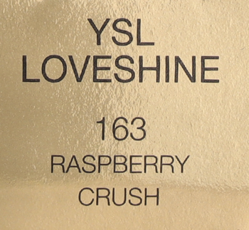 Zbliżenie etykiety produktu YSL Loveshine 163 Raspberry Crush, czarny tekst na błyszczącym złotym tle.
